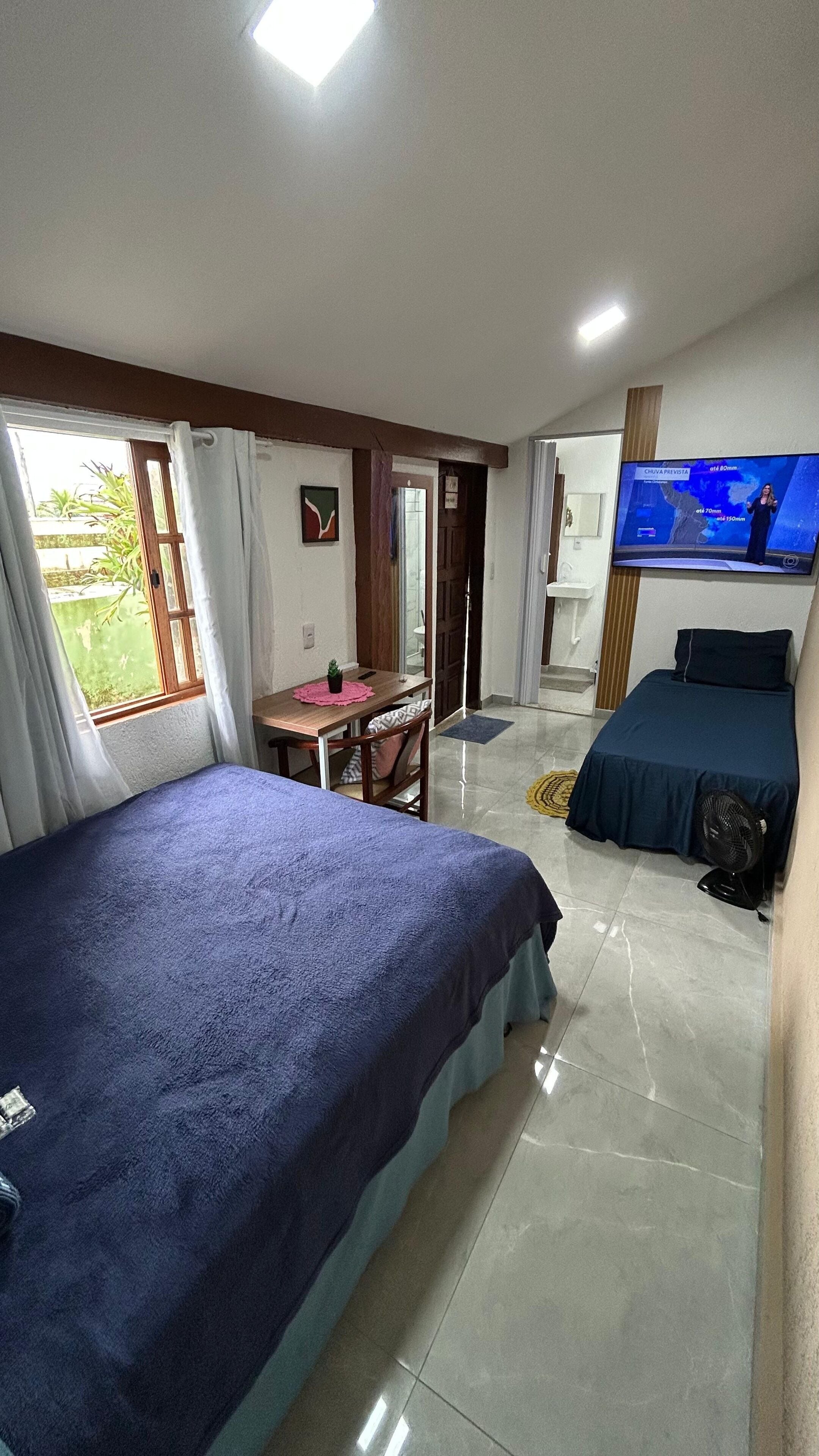 A hotel room with two beds, a desk, a television, and a window with curtains.