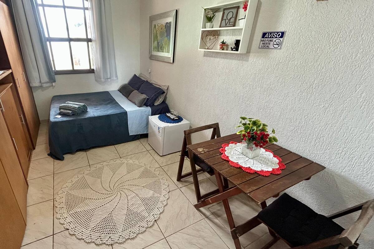 A small, cozy room with a bed, a small table with a vase of flowers, and a white wall with a sign.