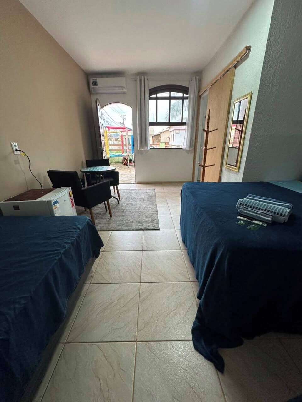 Habitación de hotel con dos camas, un escritorio y una silla. Hay una ventana con cortinas, un radiador y vistas al exterior.