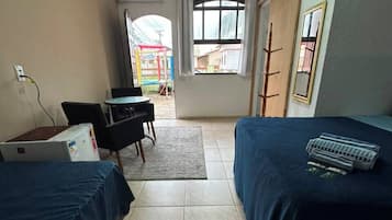Habitación de hotel con dos camas, un escritorio y una silla. Hay una ventana con cortinas, un radiador y vistas al exterior.