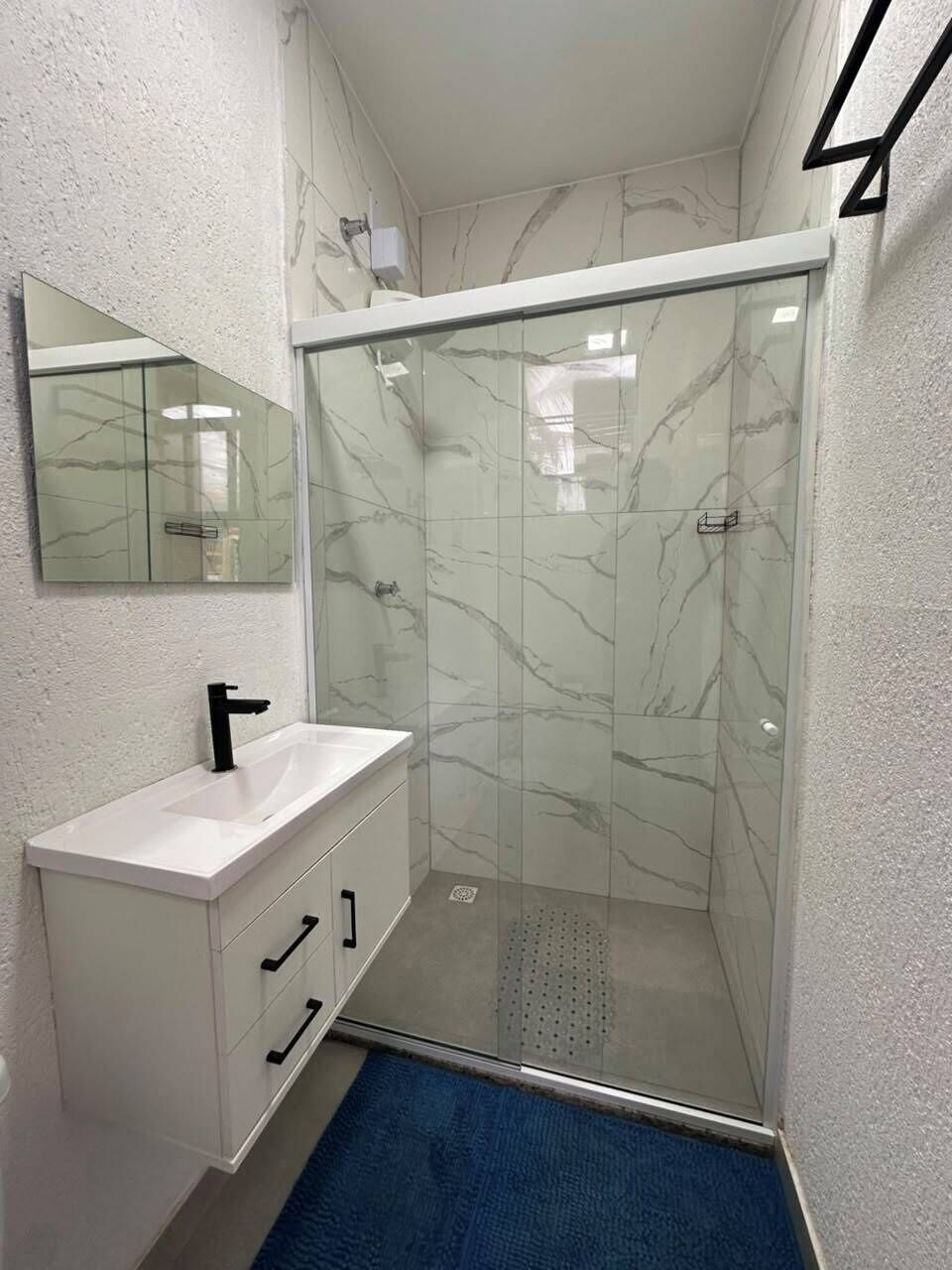 Un baño con ducha envuelta en vidrio, un lavabo blanco y un espejo encima.