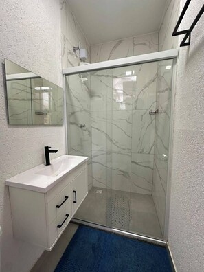 Une salle de bain avec une douche à parois de verre, un lavabo blanc et un miroir au-dessus.