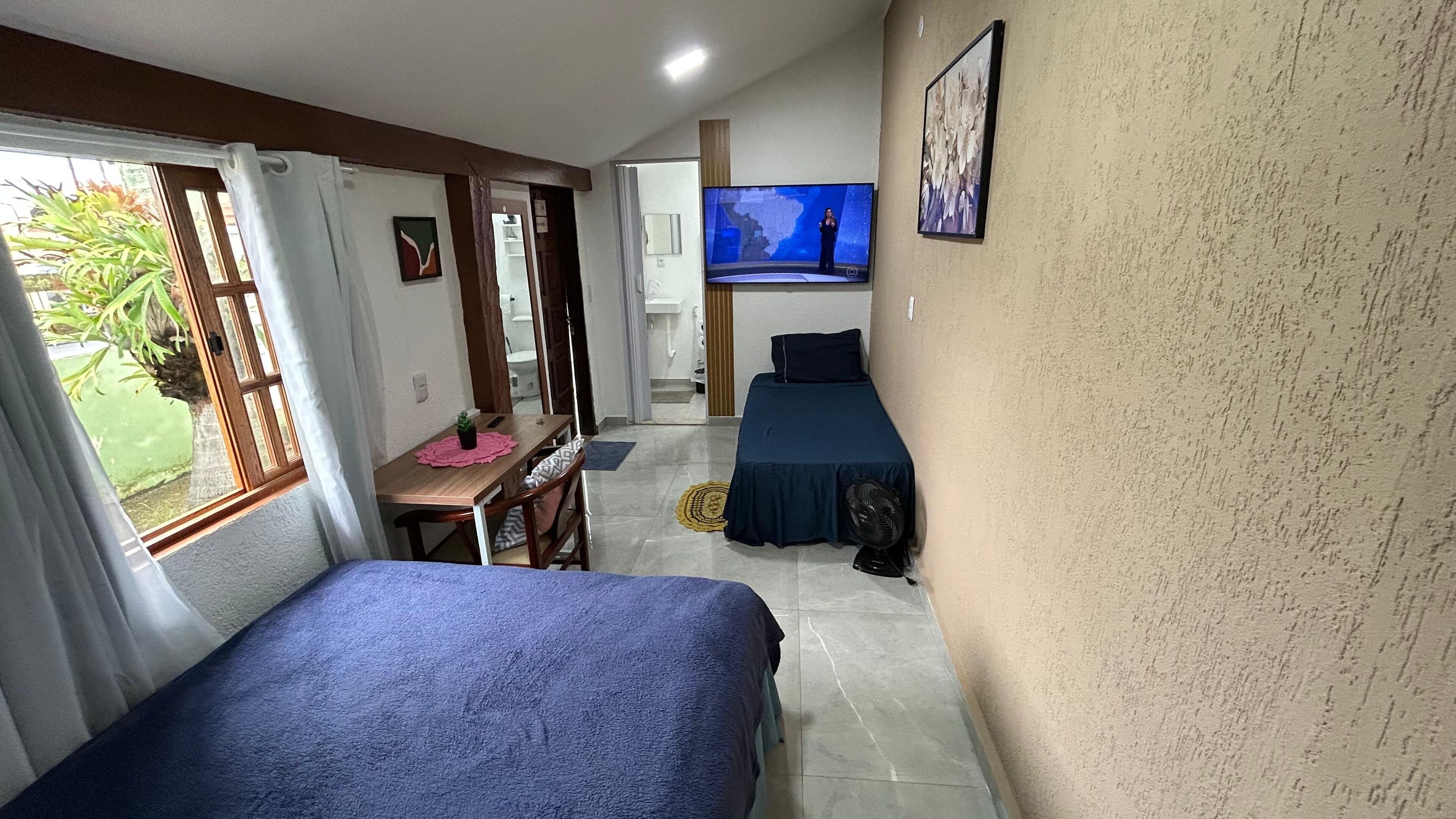 Habitación de hotel pequeña con dos camas, televisión, una pequeña mesa de comedor y un baño visible a través de una puerta abierta.