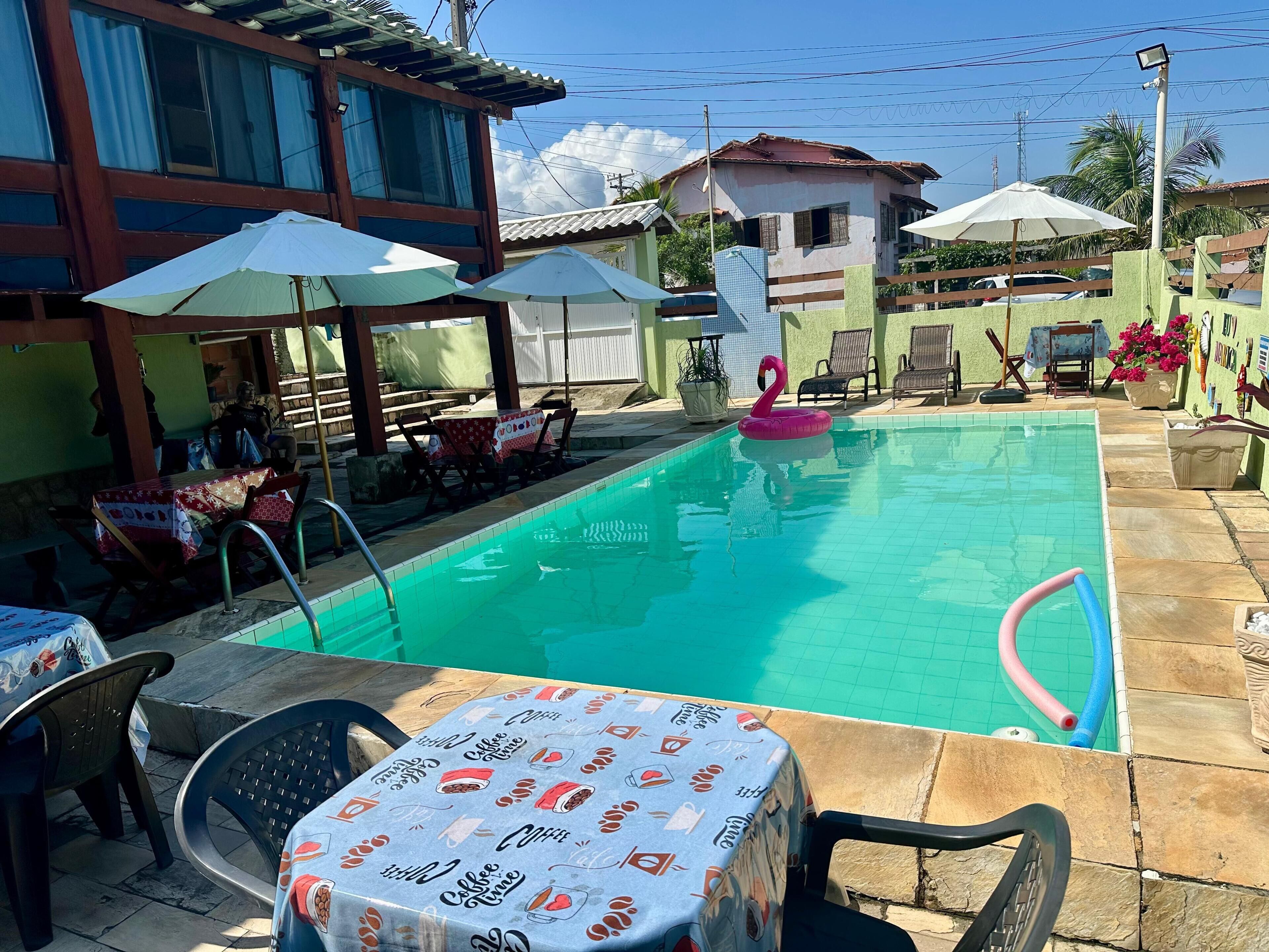 Ein Swimmingpool mit Liegestühlen und Sonnenschirmen, umgeben von einer Terrasse mit Tischen und Stühlen.