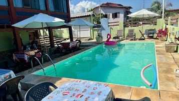 Ein Swimmingpool mit Liegestühlen und Sonnenschirmen, umgeben von einer Terrasse mit Tischen und Stühlen.