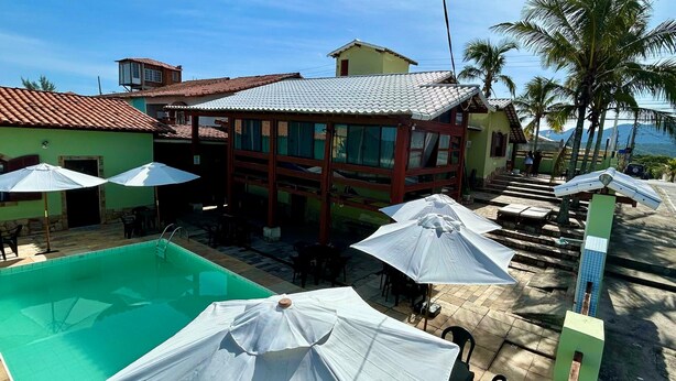 Un área de piscina con sombrillas, un edificio con tejado de azulejos y palmeras.