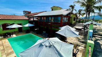 A pool area with umbrellas, a pool, and a building with a tiled roof.
