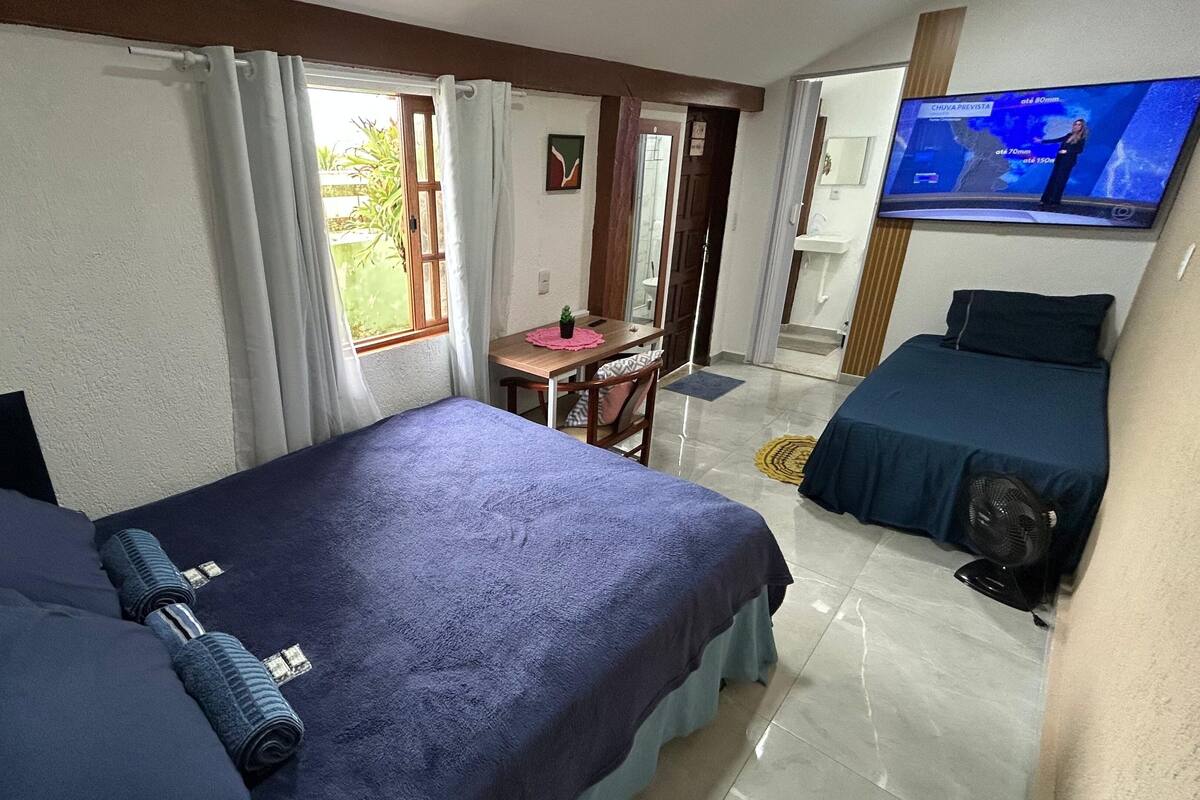A hotel room with two beds, a desk, a chair, a TV, and a fan.