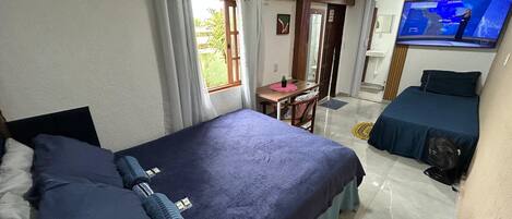 Une chambre d’hôtel avec deux lits, un bureau, une chaise, une télévision et un ventilateur.