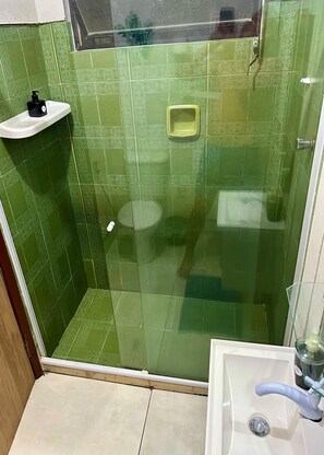 A bathroom with green patterned tiles, a glass shower enclosure, a white sink, and a soap dispenser.