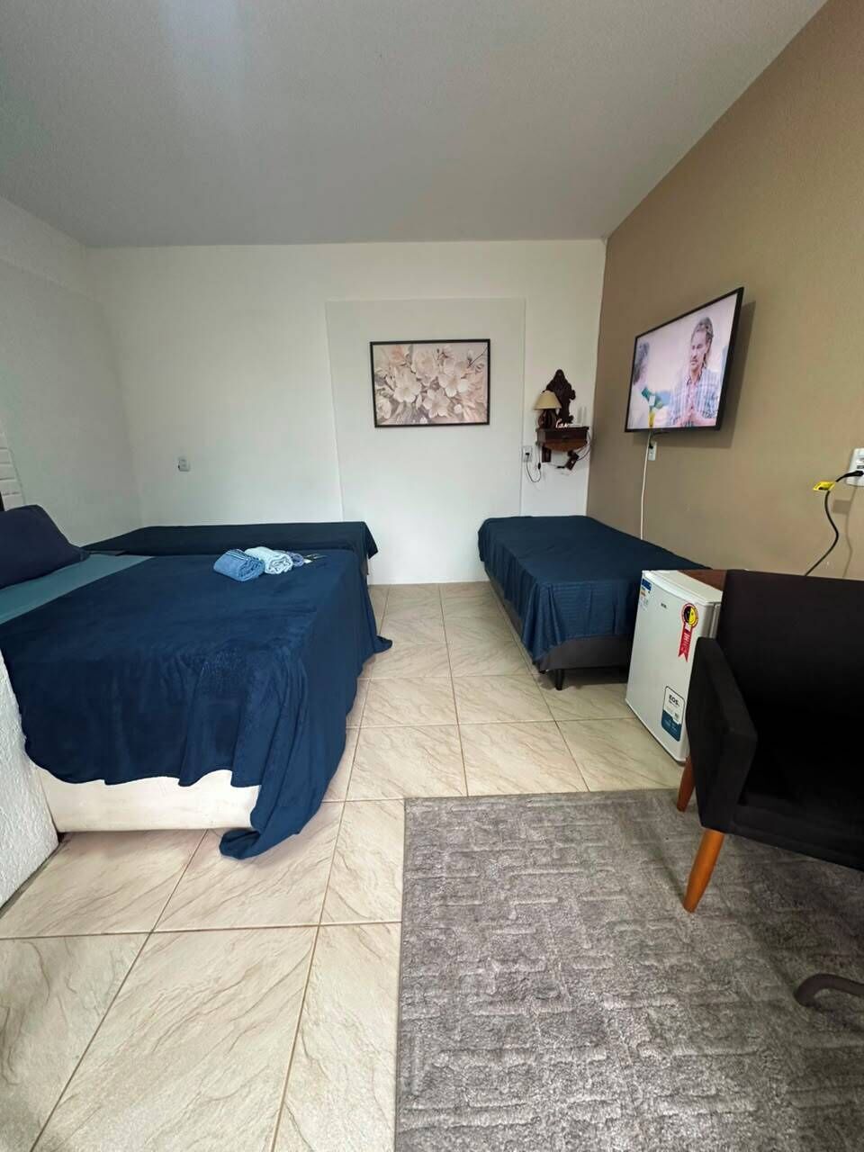 A room with two beds, a desk, a television, and a refrigerator.