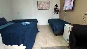 A room with two beds, a desk, a television, and a refrigerator.