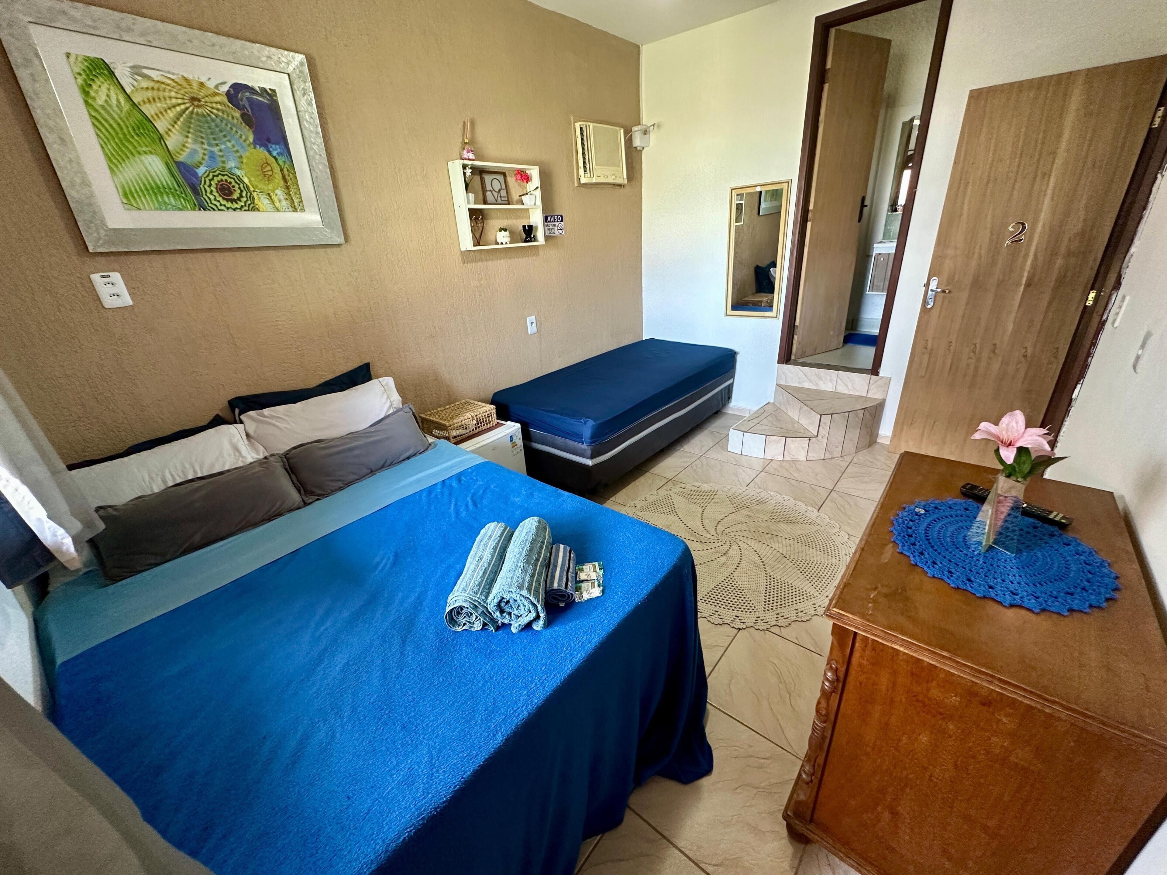 Ein Schlafzimmer mit zwei Betten, einem Nachttisch mit einer Vase, einem Spiegel und einem an der Wand montierten Regal mit Dekorationen.