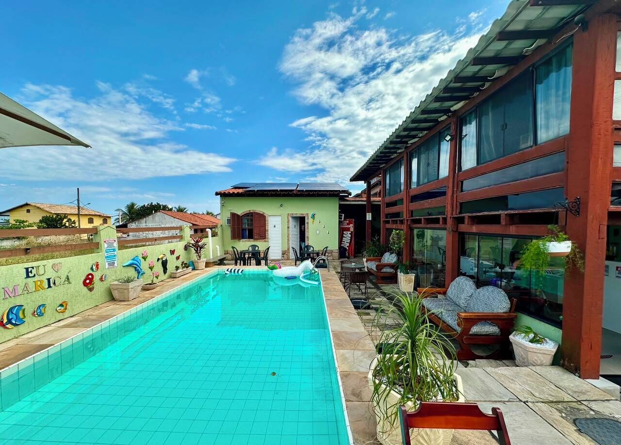 Una piscina con solárium empinado, rodeada por un edificio con amplios ventanales y un patio amueblado.