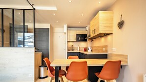 A modern kitchen with wooden cabinets, a central island with orange chairs, and a view of a snowy landscape through large windows.