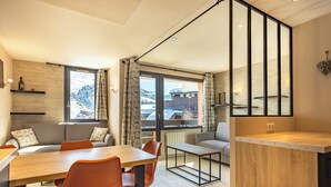A modern kitchen with a wooden dining table, orange chairs, and a view of snowy mountains through large windows.