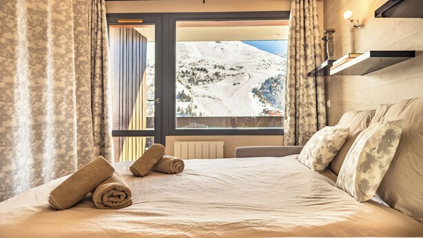 A hotel room with a bed, a view of a snowy mountain, and a window with curtains.