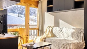 A cozy living room with a sofa, a small table, a TV, and a window with a view of a snowy landscape.