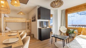 A cozy room with a bunk bed, a dining table set with plates, a small kitchen area, and a large window offering a view of the outdoors.