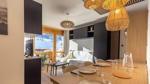 A modern dining area with a wooden table set for four, a large window with a view of a snowy landscape, and a kitchen area with a black countertop and a coffee machine.