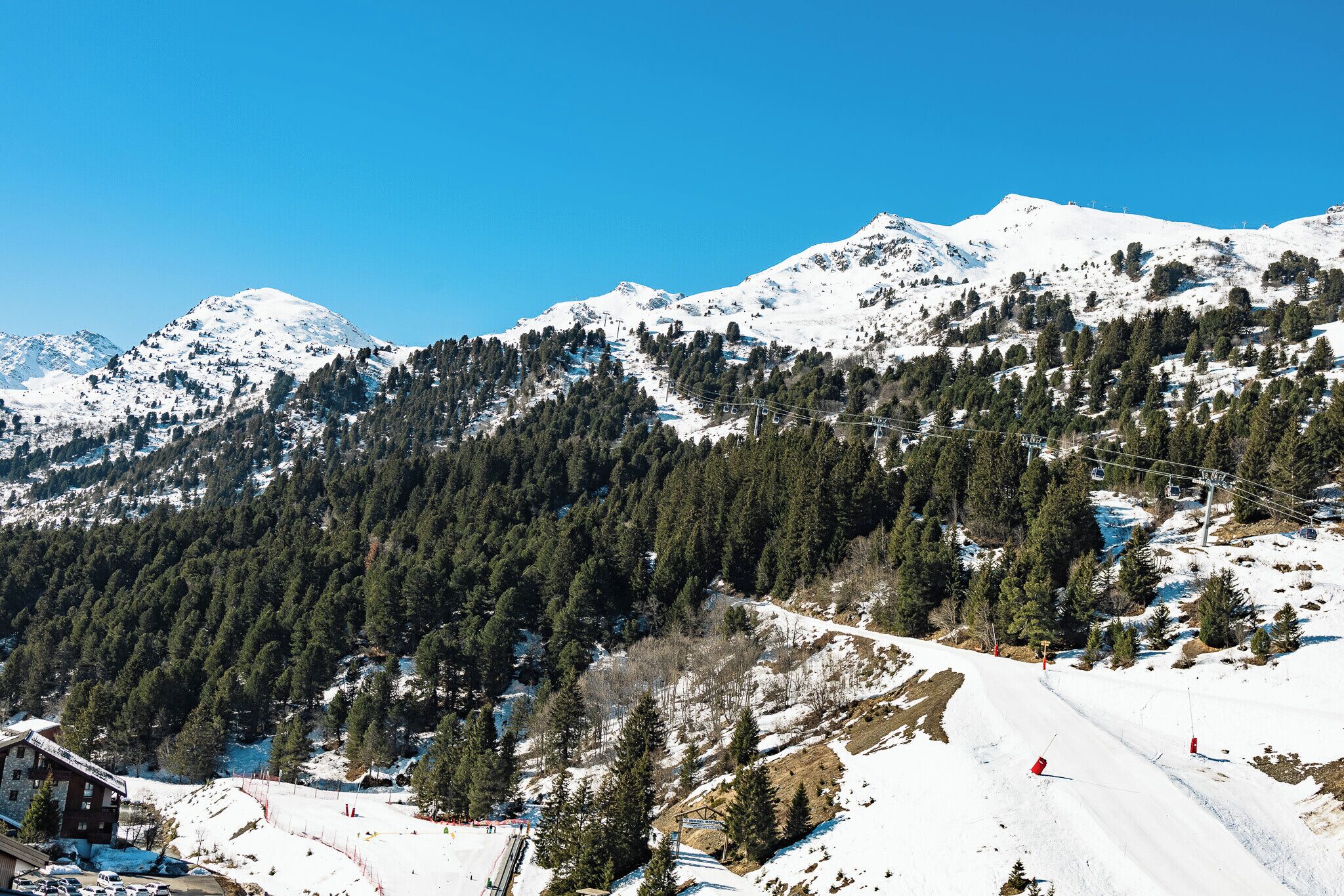 Paisaje montañoso cubierto de nieve con una pista de esquí, árboles y un edificio en la base.