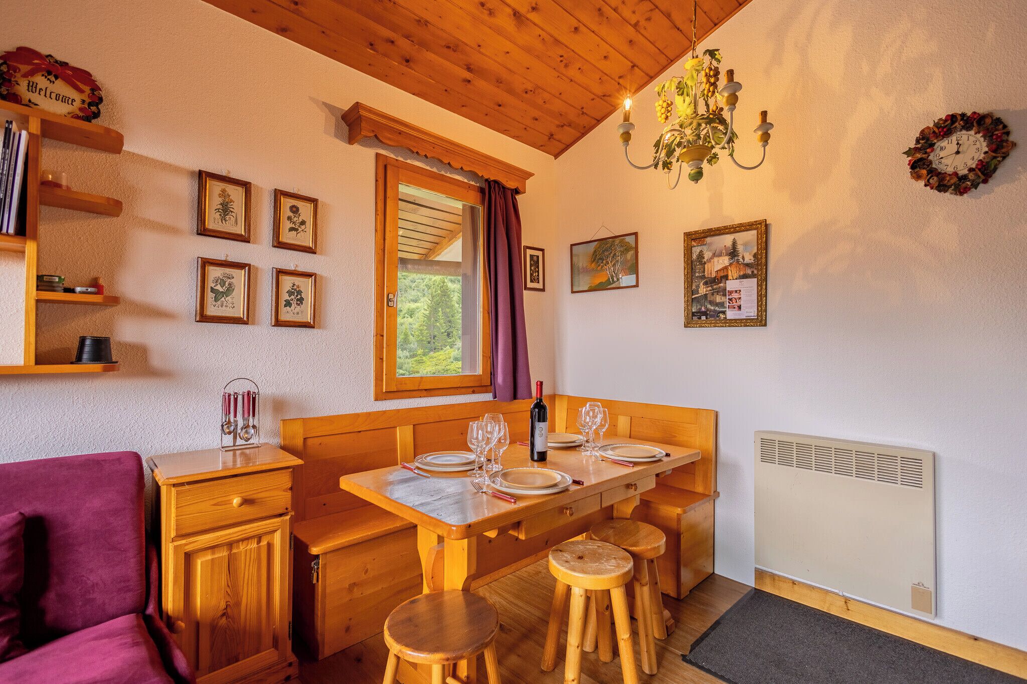 Een knus vertrek met houten meubels, een eettafel gedekt voor vier personen, een bankje en een radiator.