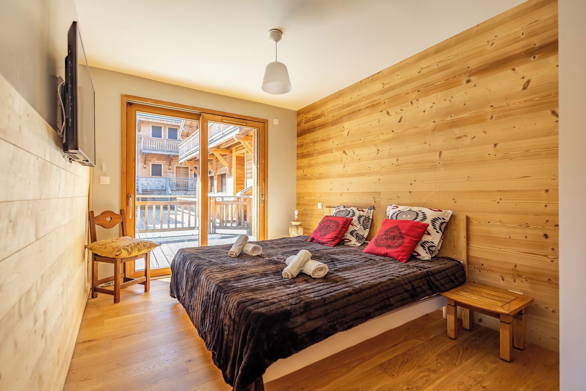 Un dormitorio con pared de listones de madera, una cama con toallas enrolladas, una silla de madera y un taburete pequeño de madera.