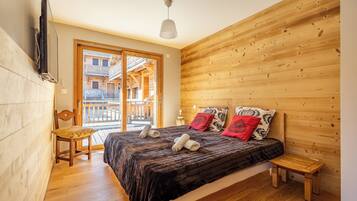 Un dormitorio con pared de listones de madera, una cama con toallas enrolladas, una silla de madera y un taburete pequeño de madera.