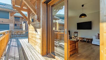 Una cabaña de madera con balcón, puerta corrediza de vidrio que da a una sala de estar con televisor, muebles de madera y vista a la montaña.