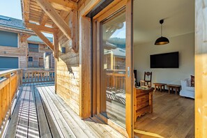 A wooden cabin with a balcony, a sliding glass door leading to a living area with a TV, wooden furniture, and a mountain view. - Chalet Olympe #101 - 5 guests (Les Allues)