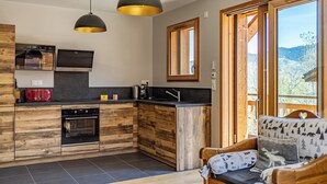 A modern kitchen with wooden cabinetry, a built-in oven, and a black countertop. There is a window with a view of the outdoors. - Chalet Olympe #101 - 5 guests (Les Allues)