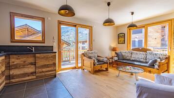 Amplia sala de estar con sofá de madera, mesa de centro de vidrio y un mueble de madera con lavamanos. Grandes ventanales ofrecen vistas al exterior.