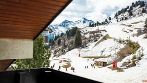 Pista de esquí con esquiadores, estructura de techo de madera y montañas nevadas.