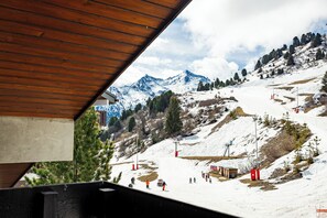 Pista de esquí con esquiadores, estructura de techo de madera y montañas nevadas.