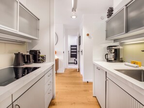 Een smalle keuken met witte kasten, een koffieapparaat en een spoelbak.