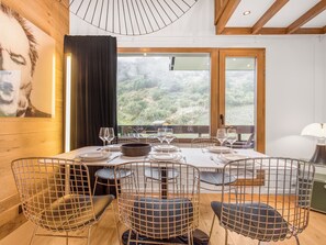 Un coin repas avec une table dressée pour quatre personnes, entouré de chaises au design épuré, donnant sur un paysage verdoyant et agrémenté d’un tableau au mur.