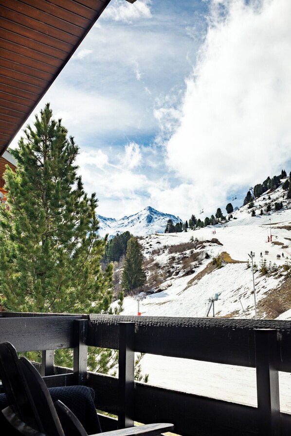 Una terraza de madera con vistas a un paisaje montañoso nevado, que incluye una pista de esquí y árboles.