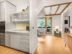 Une cuisine moderne dotée d’un grand îlot central, de planchers en bois et offrant une vue sur un jardin grâce à une porte vitrée.