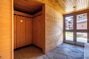 Een houten interieur met een stenen vloer, houten wanden en uitzicht op een woonwijk door een glazen deur.