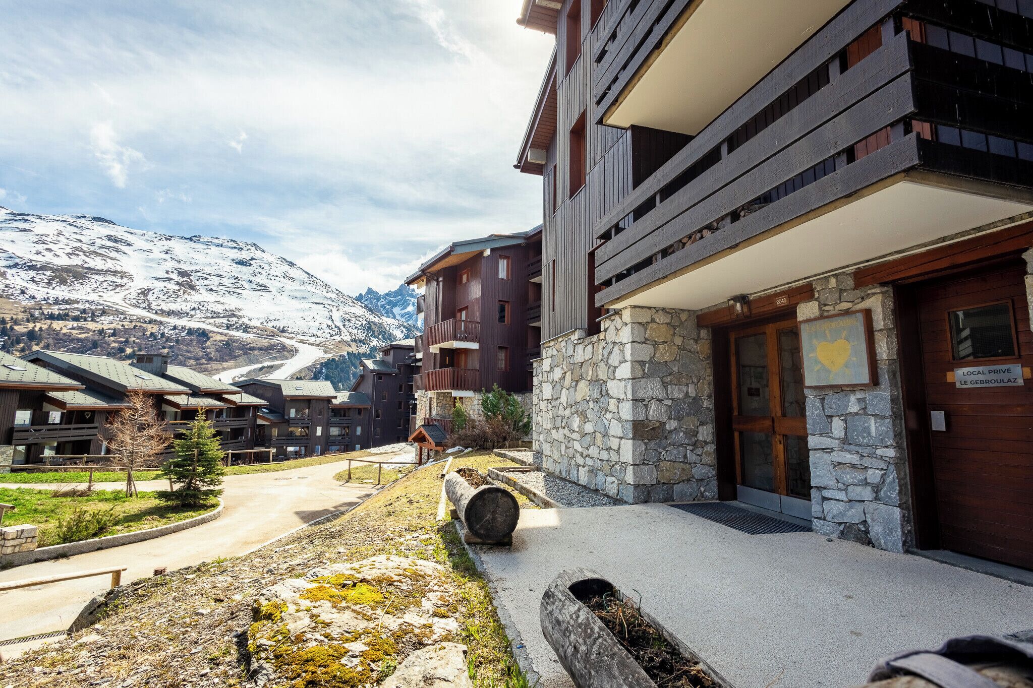 A modern building with stone and wood exterior, a stone entrance, and a view of snow-capped mountains in the background.