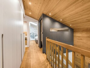 Un couloir doté d’un plancher en bois, d’une rambarde en bois et d’un mur sombre agrémenté d’une petite fenêtre.
