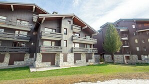 Un edificio moderno de varios pisos con balcones, cimientos de piedra y un área verde al frente.