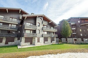 Un edificio moderno de varios pisos con balcones, cimientos de piedra y un área verde al frente.