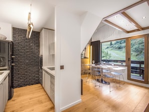 Une cuisine moderne avec un mur d’accent en briques, un coin repas offrant une vue sur l’extérieur et un plafond en bois.