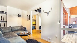 Una sala de estar moderna con un sofá seccional, una mesa de centro y un tapete negro. Se ve una ventana grande con vistas al exterior.