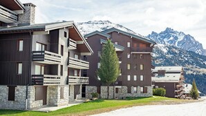 Un hotel moderno de varios pisos con balcones, fachada de piedra y vistas a montañas nevadas.