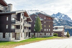 Un hotel moderno de varios pisos con balcones, fachada de piedra y vistas a montañas nevadas.
