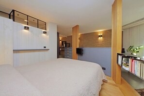 Een slaapkamer met een bed, een houten boekenkast, een bureau en een tv aan de muur.