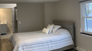 Un dormitorio con cama, ventana y un baño a lo lejos.