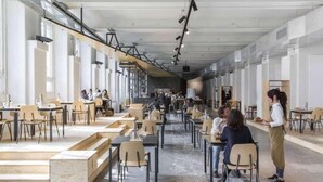 Een ruime eetruimte met hoge plafonds en natuurlijk licht, met houten tafels en stoelen, en een modern industrieel design.